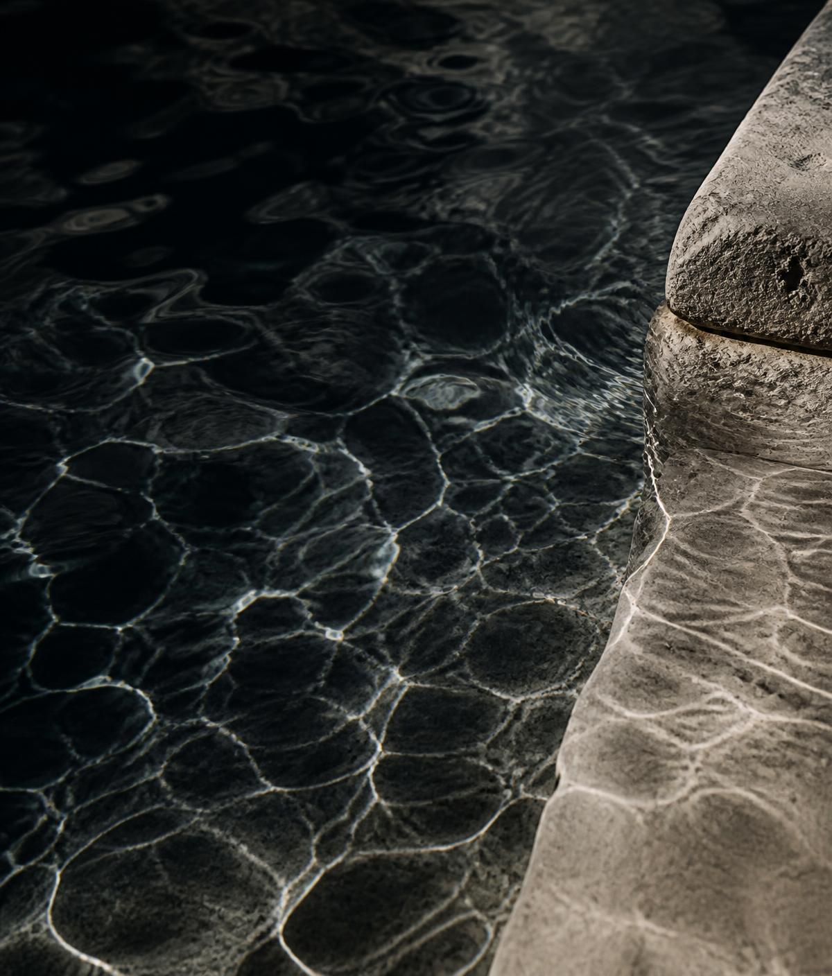 Dark water surface with light caustics beside pale stone